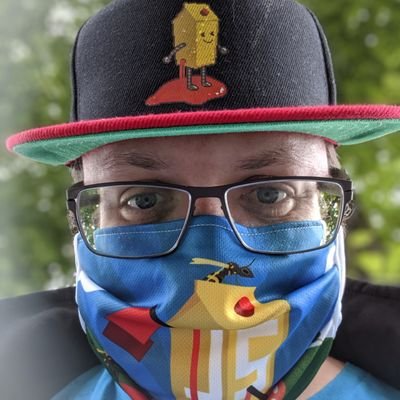 Headshot of Björn wearing glasses, a Juice Shop cap, and a Juice Shop mask. Only his eyes and eyebrows are not covered. He is outside in front of a green bush.